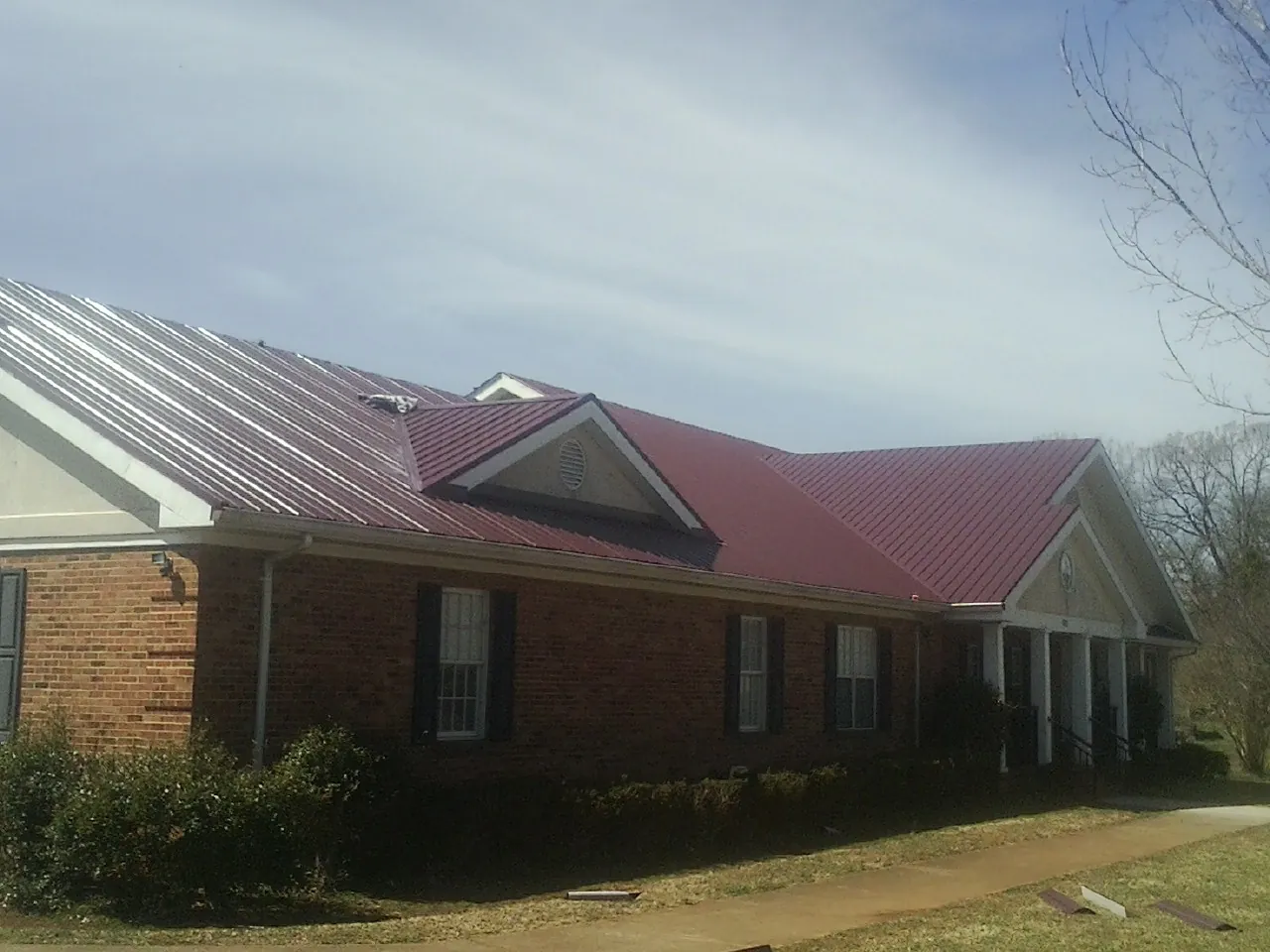 Red metal roof with gabled entries on a long brick building, from a Hail Damage Roof Repair job in National Park