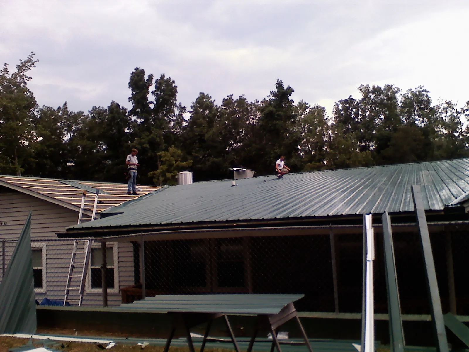 Two roofers installing green metal panels above a covered porch in National Park