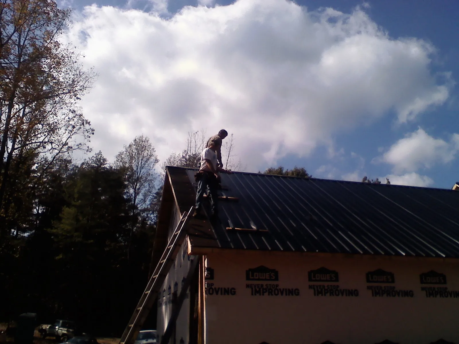 Roofer fastening dark metal panels high against a cloudy sky, from a Roof Inspection job in National Park