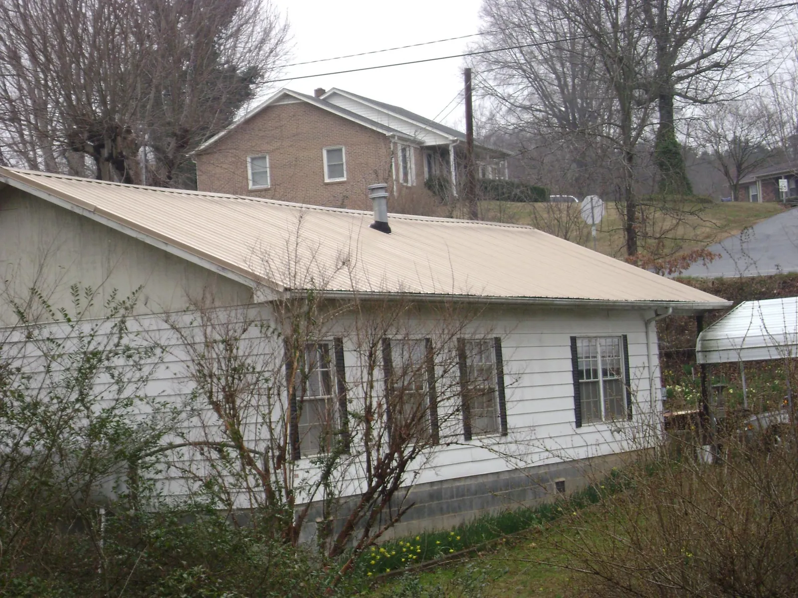 Tan metal roof on a white sided house set into a hillside — Commercial Roofing by Roofing Brothers in National Park